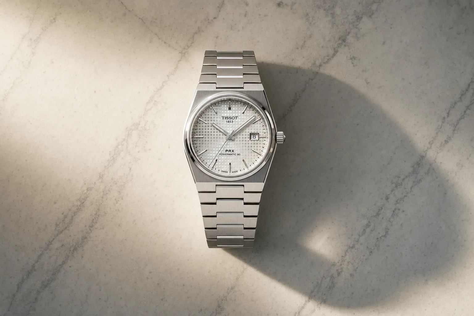 Tissot PRX de aço sobre uma superfície de mármore claro, com luz lateral dura