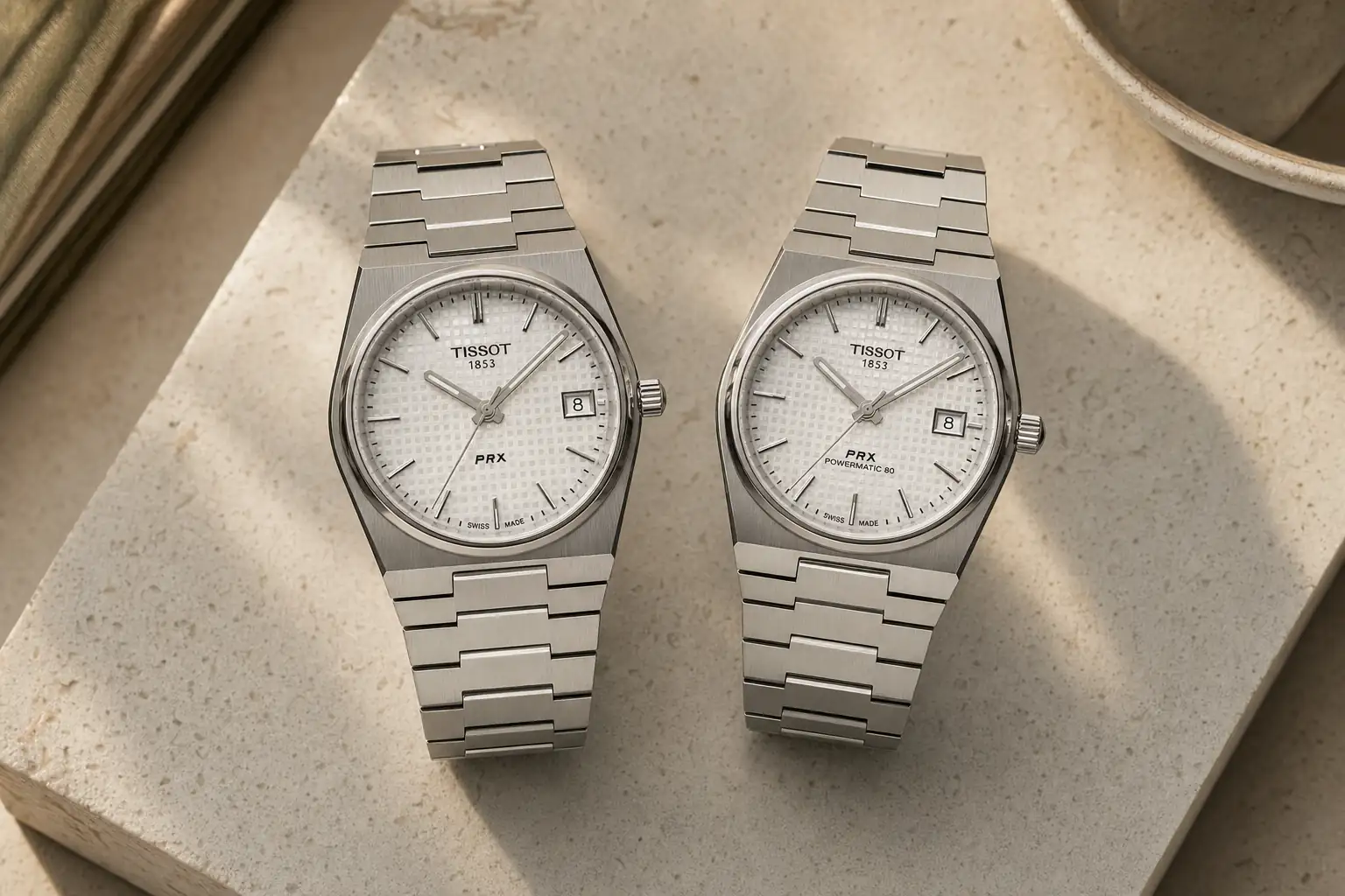 Dois Tissot PRX lado a lado sobre pedra clara, um com fundo de vidro e outro com fundo fechado
